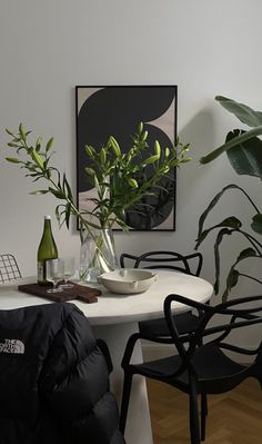 a white table topped with a vase filled with green plants next to a black chair