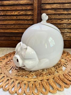 a white ceramic pig on a doily with wood shutters in the backround