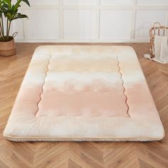 a pink and white dog bed sitting on top of a wooden floor next to a potted plant