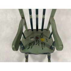 a green chair with painted flowers on the back and arms, sitting against a white background