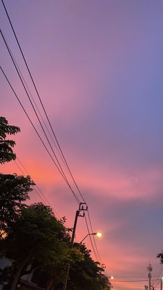 the sky is pink and purple as the sun goes down in the distance behind some power lines