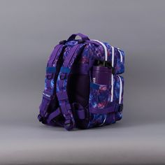 a purple and blue backpack sitting on top of a gray floor next to a wall