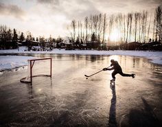 a person on an ice rink playing with a hockey stick and the sun is setting in the background