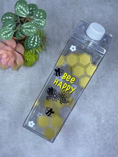 a water bottle with bee happy on it next to a potted plant and flowers