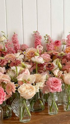 a bunch of vases filled with pink and white flowers on a wooden table next to a wall