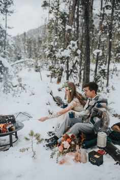 two people sitting in the snow next to an open fire pit with food on it