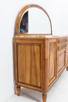 an old wooden dresser with a mirror on it's sideboard and legs, against a white wall