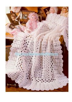 a crocheted afghan with two dolls sitting on the floor in front of it