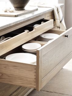 an open drawer with plates in it on the counter next to a bowl and utensils