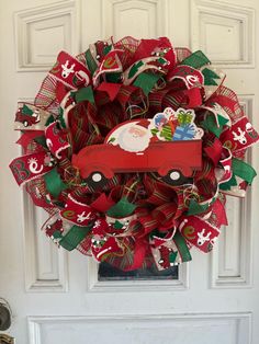 a christmas wreath with a red truck and santa clause on it, sitting in front of a white door