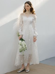 a woman in a white dress is holding a bouquet and standing against a wall with her hands on her hips