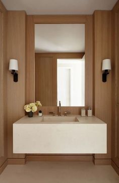 a bathroom sink sitting under a mirror next to two lights and a vase with flowers on it