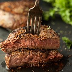 a fork sticking out of some meat on top of a black surface with parsley in the background