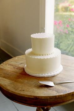 a three layer white cake sitting on top of a wooden table