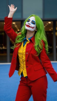 a woman with green hair wearing a red suit and yellow shirt is holding her hand up in the air