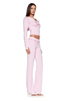 A woman stands posing in a full-length, side view. She is wearing a light pink, long-sleeved top with J'Adore written on it and matching pastel pink BLARE TRACKPANT from I.AM.GIA. She has long, straight hair and is wearing white, open-toe platform sandals. I Am Gia Pink Set, Pink Iamgia Set, Iam Gia Set, Pink Sets Outfit, Streetwear Fashion Pink, 2 Piece Lounge Set Outfit, Pink Track Pants Outfit, Cute Sets Two Pieces, Coquette Soft Style