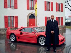 a man standing next to a red sports car in front of a white building with red shutters