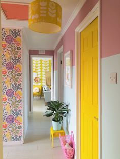 the hallway is decorated in bright colors and has a yellow door, potted plant, and pink walls