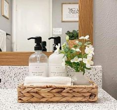 a bathroom counter with soap, lotion and flowers in a wicker basket on it