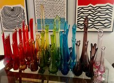 there are many different colored vases on the glass table in front of art work