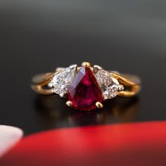 three stone ring sitting on top of a black surface with red and white stones in the middle