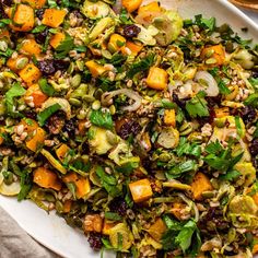 a white platter filled with vegetables and nuts on top of a table next to bread