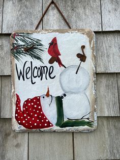 a welcome sign hanging on the side of a building with a snowman and cardinal