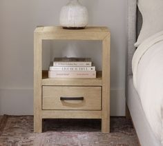 a nightstand with two books on it next to a bed