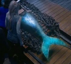 a woman standing next to a large blue fish on top of a wooden floor covered in chains