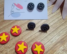 three buttons with yellow stars on them sitting next to a pair of black and red earrings