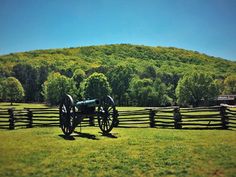 an old cannon sitting on top of a lush green field next to a wooden fence