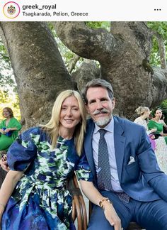 a man and woman sitting next to each other in front of a tree with people standing around