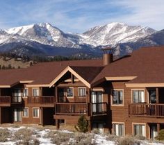 an apartment building in the mountains with snow on the ground and mountain range behind it