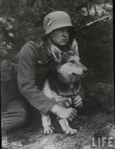 a man kneeling down next to a dog wearing a helmet and holding something in his hand