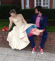 a man and woman dressed in wedding attire sitting on brick wall next to each other