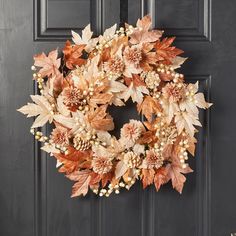 a wreath is hanging on the front door with autumn leaves and berries around it,