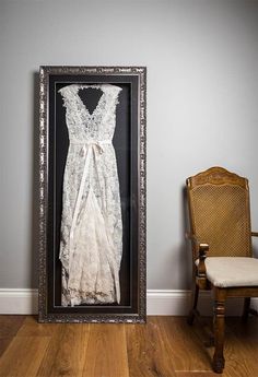 an old fashion dress in a frame on the floor next to a chair and wall