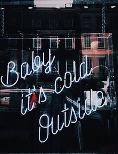 the words baby, it's cold outside are written in neon letters on a glass window