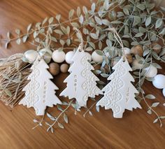 three decorated christmas trees sitting on top of a wooden table next to eggs and greenery