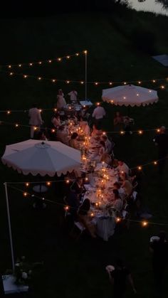 an overhead view of people sitting at tables with umbrellas and lights strung across the lawn