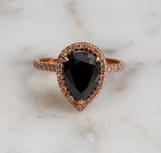 a close up of a black diamond ring on a white marble surface with diamonds around it