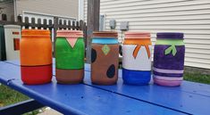 five different colored cups sitting on top of a blue picnic table in front of a house