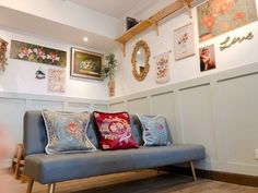 a blue couch sitting in front of a wall with pictures on the walls and paintings above it