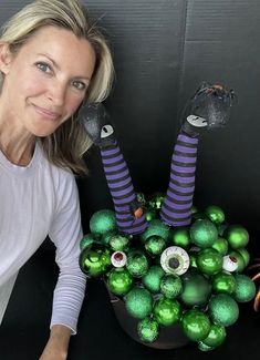 a woman sitting in front of a vase filled with green and purple ornaments on top of a table