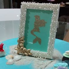 a blue table topped with a frame filled with sea shells and seashells next to a starfish