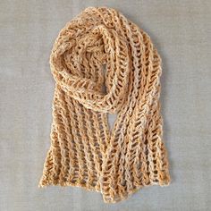 a crocheted scarf laying on top of a white cloth covered in light brown yarn