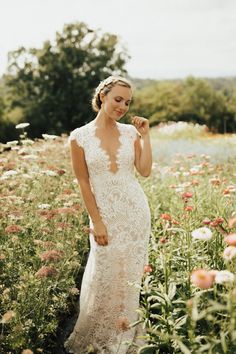 a woman standing in a field of flowers wearing a wedding dress with an open back