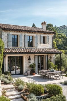 an outdoor dining area in front of a large stone house with white shutters on the windows