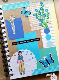 an open notebook with paper and stickers on the pages that include flowers, butterflies, and words