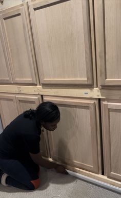 a woman kneeling down in front of wooden cabinets